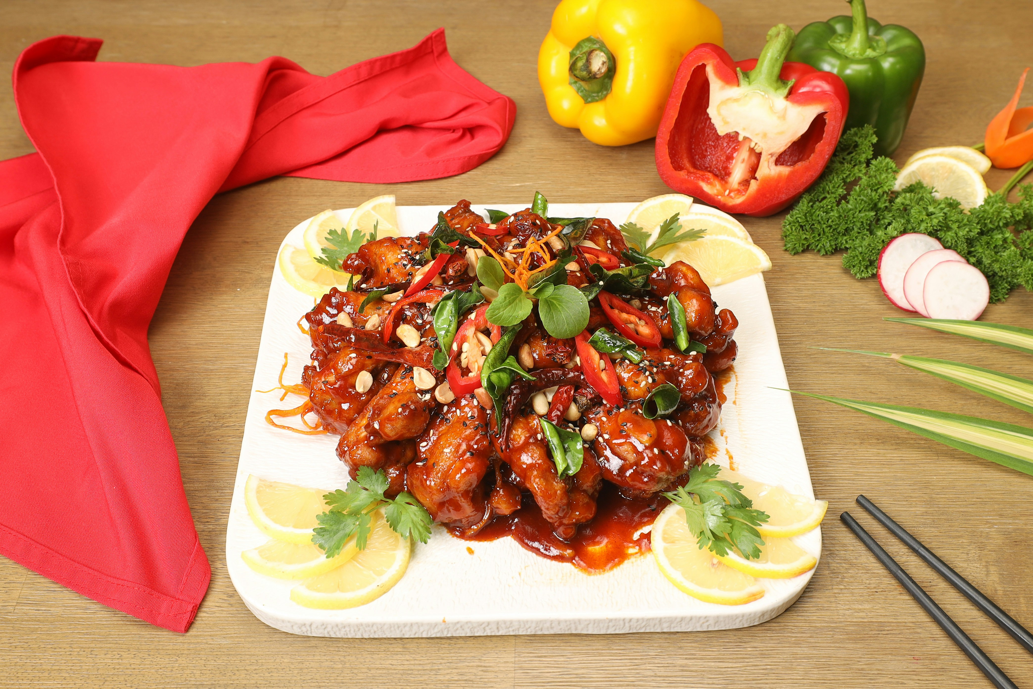 Dry chilli chicken with peppers, lemon slices and fresh herbs on a white plate