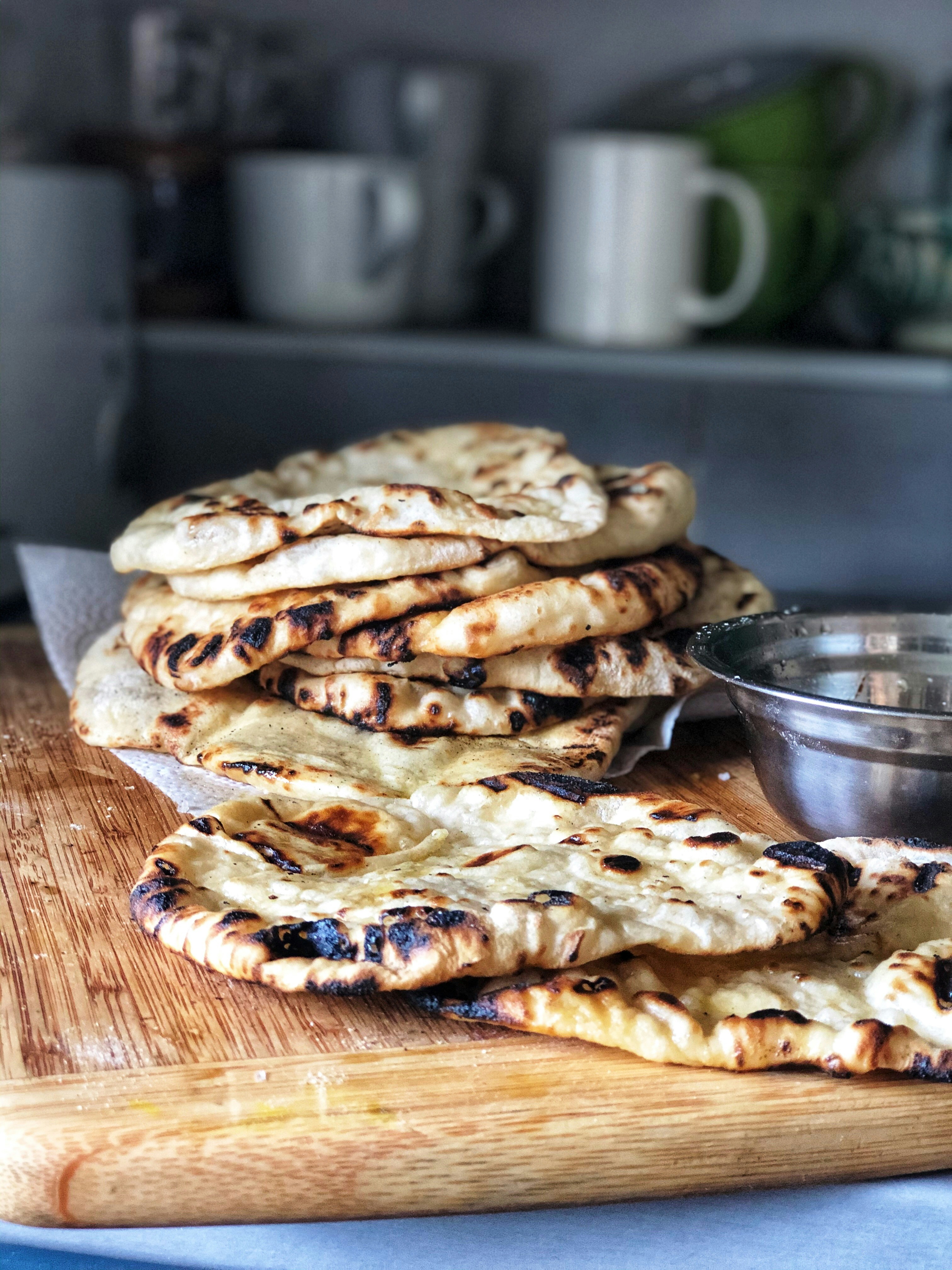 Stack of freshly charred naan flatbreads on a wooden board