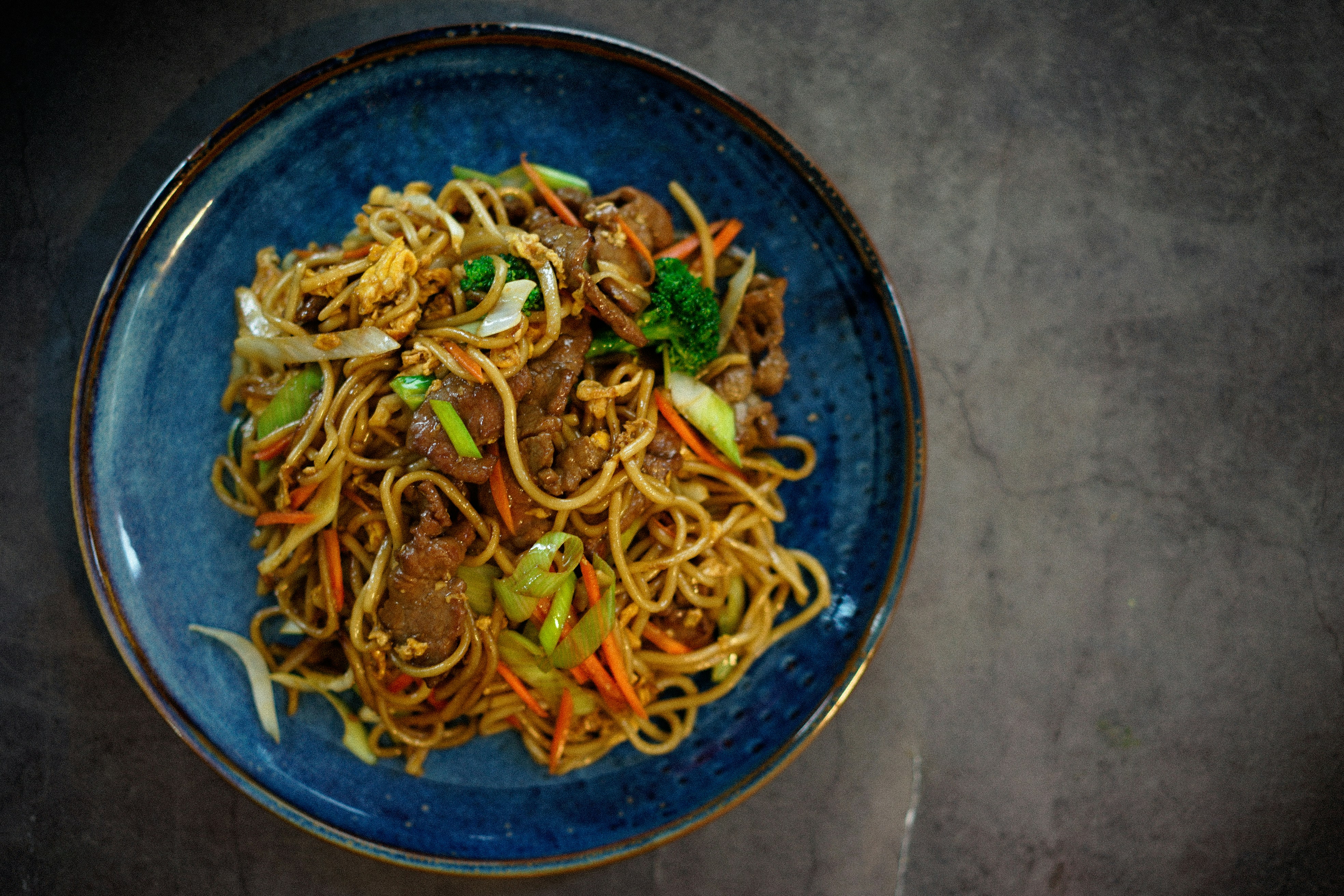 Stir fried noodles with beef and vegetables on a blue ceramic plate