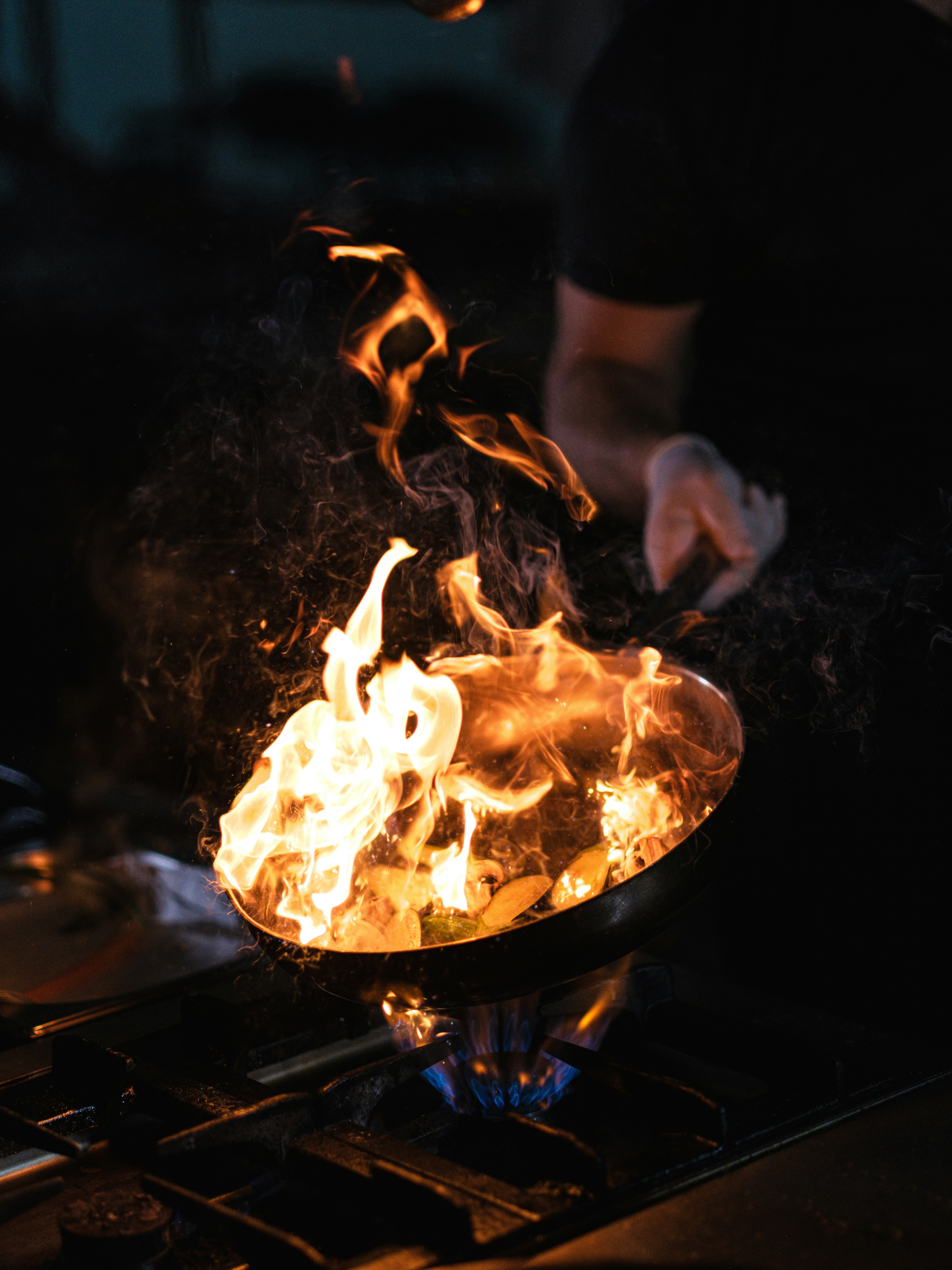 Chef cooking over a blazing wok with dramatic flames in a restaurant kitchen